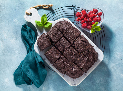 chocolate vegan brownie pie with tahini and fresh raspberries on a blue background