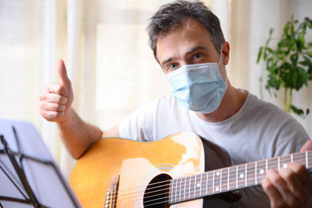 istock Man with guitar and mask with ok gesture at home 1249237765