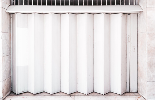 A Garage or other entrance closed metal gate texture with white vertical fanfold lines of the door; front view of an accordion-folded painted door of big gates on the street common in Lisbon, Portugal