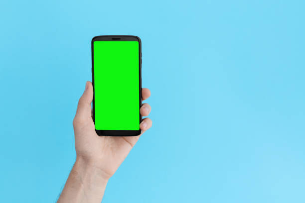 istock Smartphone with a green screen in left hand on an light blue background. 1249250953