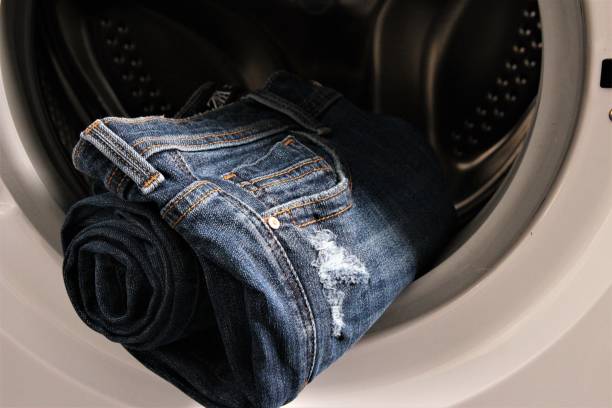 Blue jean trouser roll on lid of washing machine stock photo