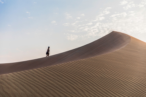 woman walking to the top of a dune in the middle of the desert and clouds