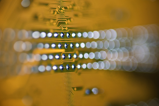 Abstract view of a yellow printed circuit Board with a narrow selective focus and shiny pins bokeh background