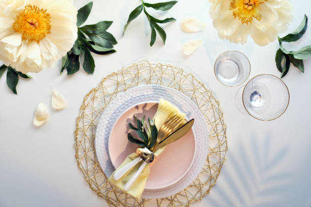 istock Contemporary table setting with peony flowers and golden utensils on white table. Modern trendy flat lay, top view on dinner table decorated in yellow, cream and green colors. Pentecost celebration. 1249257711