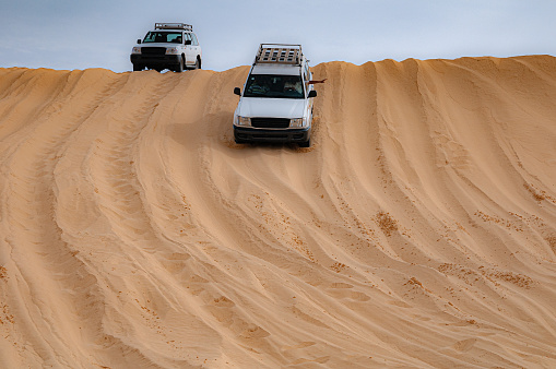 White suv on the red sand dunes during a safari in Sahara Desert in Tunisia