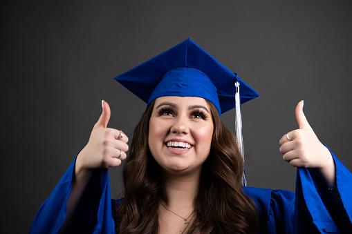 Smiling young hispanic woman celebrating her graduation posing with her thumbs up