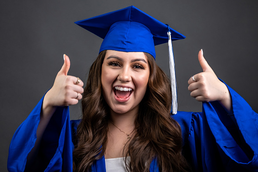 Smiling young hispanic woman celebrating her graduation posing with her thumbs up