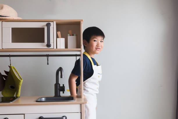 istock Boy wearing apron steps out from behind toy kitchen 1249260114