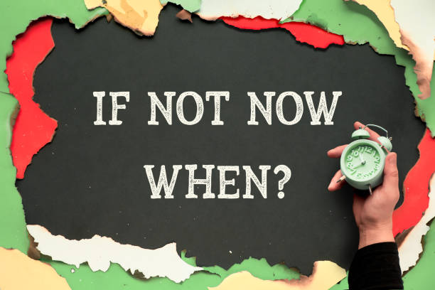istock If not now when? Text on black paper, hand hold alarm clock. Burnt burned multicolor paper background. 1249260766