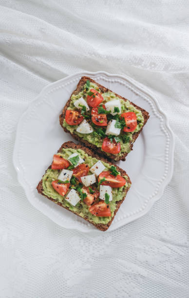 Bruschetta toast with guacamole and tomatoes. Bruschetta toast with guacamole and tomatoes, sea salt and herbs on dark bread and a white plate, healthy nutrition. High quality photo egg cherry tomato rye stock pictures, royalty-free photos & images