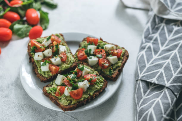 Bruschetta toast with guacamole and tomatoes. Bruschetta toast with guacamole and tomatoes, sea salt and herbs on dark bread and a white plate, healthy nutrition. High quality photo egg cherry tomato rye stock pictures, royalty-free photos & images