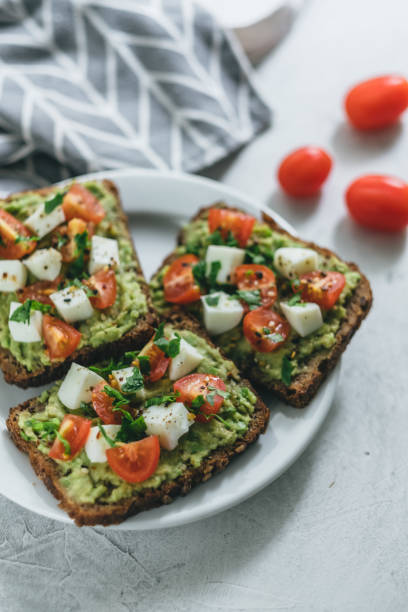 Bruschetta toast with guacamole and tomatoes. Bruschetta toast with guacamole and tomatoes, sea salt and herbs on dark bread and a white plate, healthy nutrition. High quality photo egg cherry tomato rye stock pictures, royalty-free photos & images