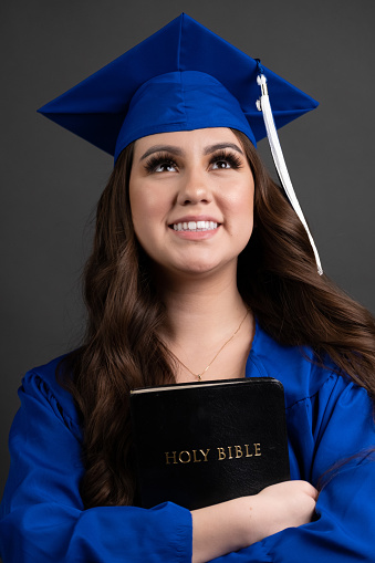 Smiling young hispanic woman celebrating her graduation holding a bible