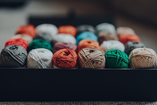 Close up of a box full of 24 different coloured skeins of amigurumi cotton yarn, selective focus on the closest row.