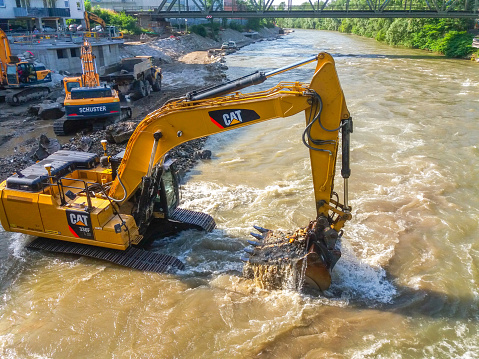 Graz/Austria - June 12, 2019: Yellow CAT industrial excavator working in the river, extracting sand and pebbles on construction site