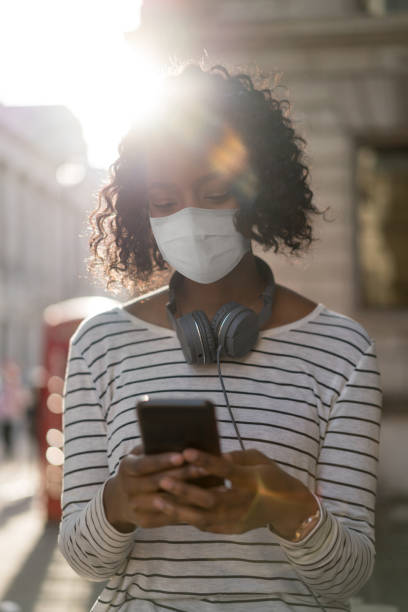 istock YoAfrican American woman outdoors wearing a facemask while texting on her cell phone ung woman on the street texting on her cell phone 1249276386