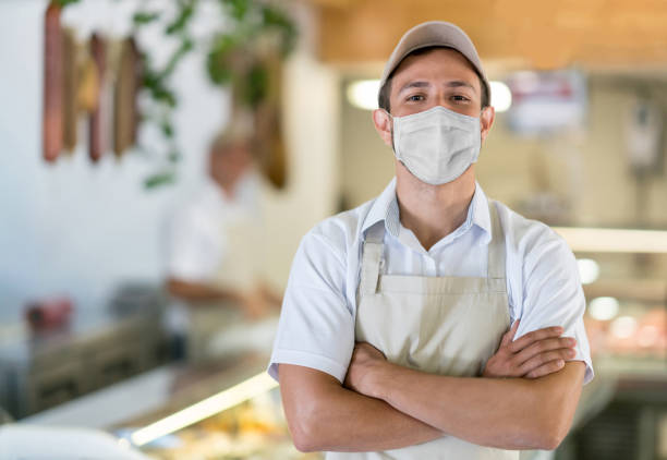 hombre que trabaja en la carnicería con una máscara facial para evitar el coronavirus - delicatessen beef meat raw fotografías e imágenes de stock