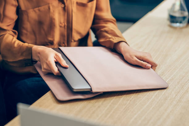 mani di un'imprenditrice che toglie il suo computer portatile dalla manica sulla sua scrivania - manica foto e immagini stock