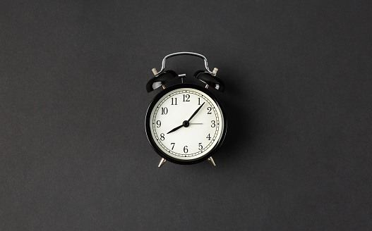 Classic alarm clock on abstract dark black minimal background with room for text. Simple time concept.
