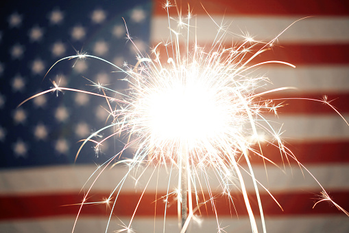 Lit sparkler burning in front of American Flag