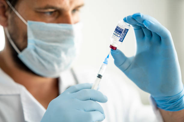 Male doctor drawing the Measles, Mumps, Rubella (MMR) Vaccine Close up of a medical professional holding a syringe drawing vaccine from a vial to prepare for injection measles stock pictures, royalty-free photos & images