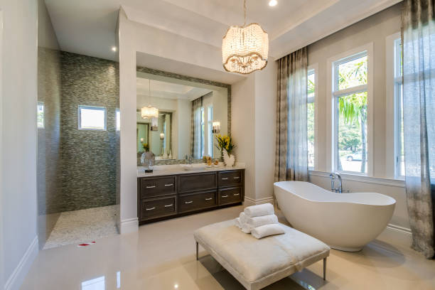 Private master bathroom suite in Florida home Freestanding tub and ottoman stool in center of bathroom with shower in the background light fixture stock pictures, royalty-free photos & images