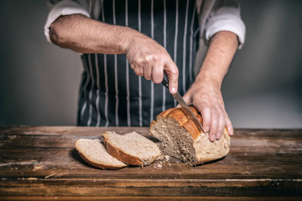 istock Baker cutting rye bread into slices at bakery on wooden table 1249305378