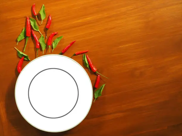 "nWhite empty plate with chilies and basil The background is real solid wood."nFood show concept"nSuitable for advertisement of food and display signs.