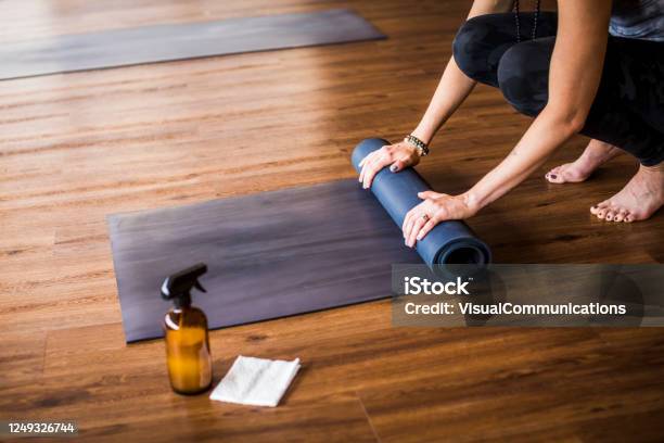 Woman Rolling Up Yoga Mat With Sanitizer Nearby Stock Photo - Download Image Now - Cleaning, Exercise Mat, Yoga Studio