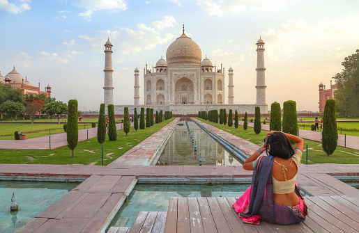 Agra, India, May 30,2019: Young female tourist in traditional Indian dress clicking photographs of the Taj Mahal at sunrise at Agra, India