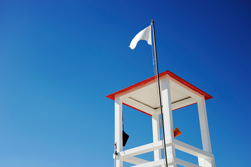 Lifeguard wooden tower on the beach against blue sky. Megaphone and other tools hang from the tower. The white flag waving on the roof.Copy space for text. Risk and rescue concept.