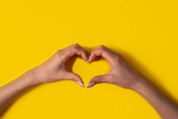 istock heart making woman's hands with manicure on yellow background, top view 1249341248