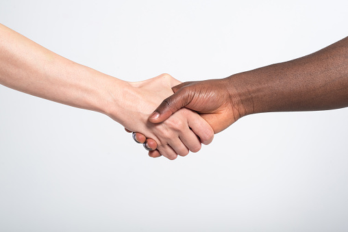 Anti racist, anti discrimination studio shot of unrecognizable, mixed race two people shaking hands.