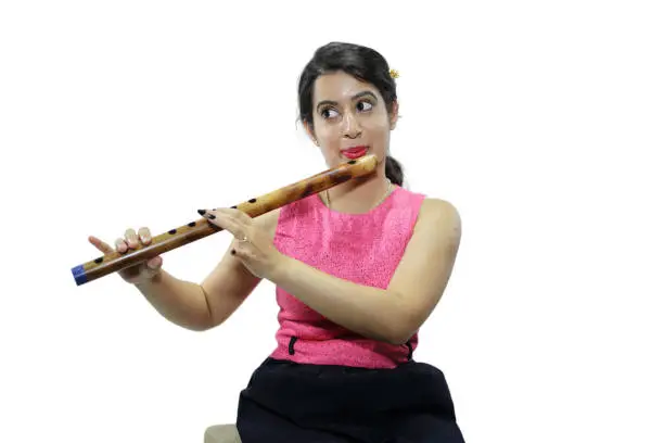 Young woman in casual wear playing bansuri, a kind of traditional Indian musical instrument.