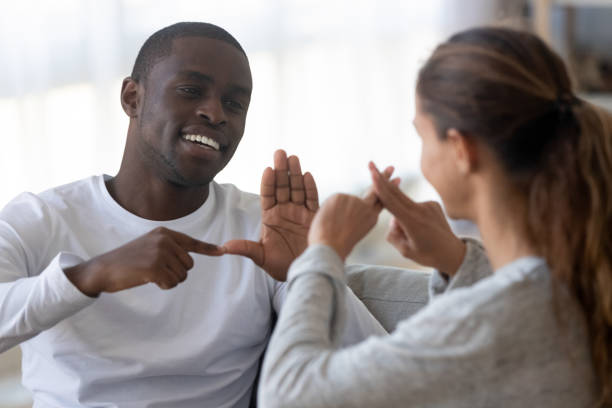 Smiling multiracial friends talk using sign language Smiling african American man sit on couch show hand gestures talking with female friend at home, international disabled hearing impaired couple or spouses use sign language communicating deafness photos stock pictures, royalty-free photos & images