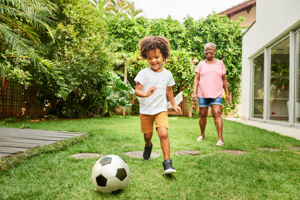 Shot of a little boy playing football with his grandmother in backyard