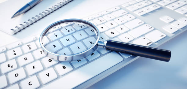 Magnifying Glass on Computer Keyboard Magnifying glass lying on a white computer keyboard - Searching Information Concept byte photos stock pictures, royalty-free photos & images