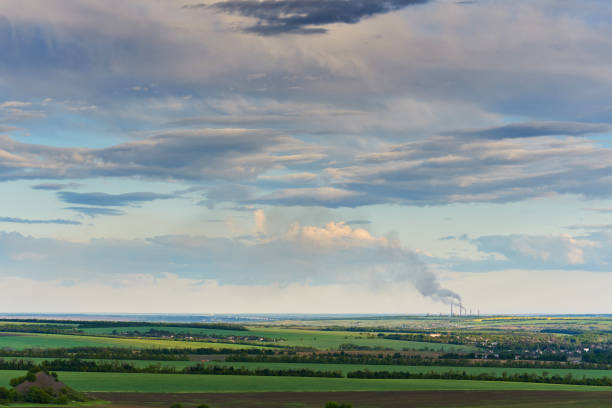 Blue sky with clouds over green fields and a thermal power plant with a smoking chimney.