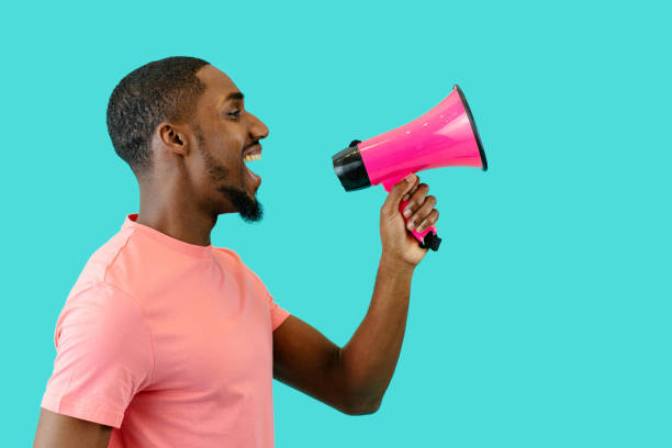 portret uśmiechniętego młodego mężczyzny przemawiającego przez megafon z otwartymi ustami - marketing megaphone advertise listening zdjęcia i obrazy z banku zdjęć