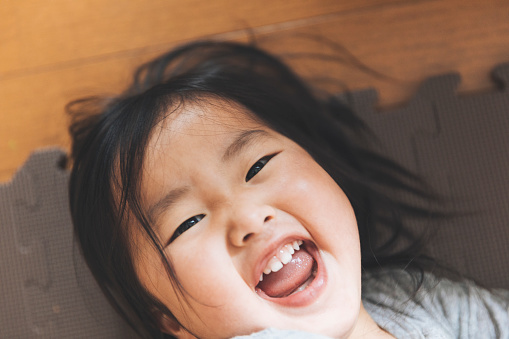 Asian baby girl lying down on floor and laughing.