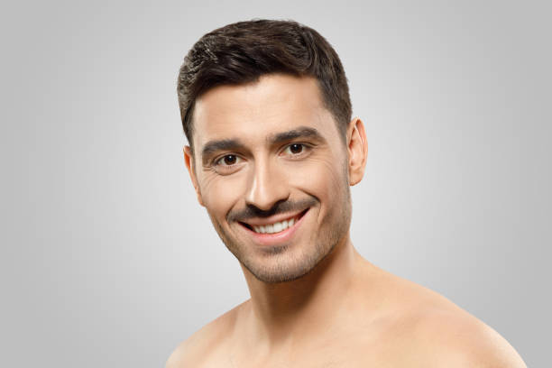 istock Young handsome guy with dark hair and bristle, smiling happily while standing without shirt, concept of men beauty, isolated on gray background 1249362001
