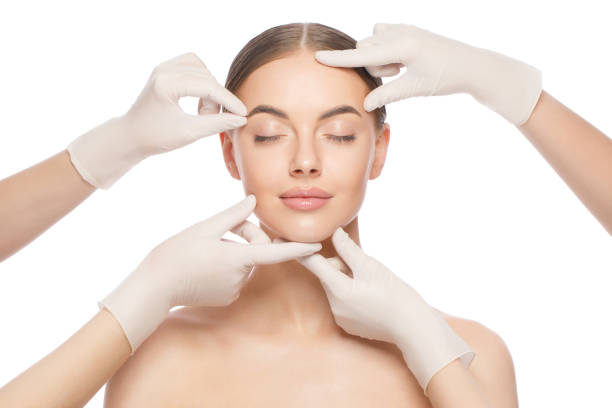 close-up portrait of young woman standing with naked shoulders and neck, face is touched by beauticians in gloves, preparing her for plastic surgery procedures, isolated on white background - spa treatment beautiful healthcare and medicine white imagens e fotografias de stock