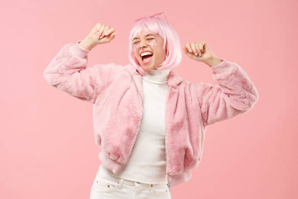 Excited teenage girl dancing and cheering to sounds of music, wearing fluffy fur coat and colored hair at party, isolated on pink background Excited teenage girl dancing and cheering to sounds of music, wearing fluffy fur coat and colored hair at party, isolated on pink background pink hair stock pictures, royalty-free photos & images