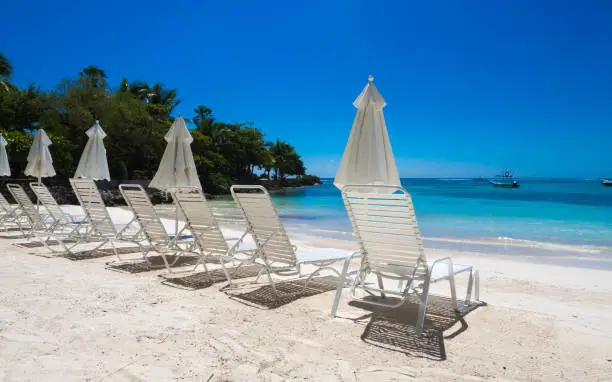 a group of empty beach chairs inviting for a sunbath at a white beach in front of crystal clear water in the caribbean
