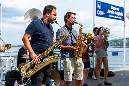 Geneva, Switzerland - August 24, 2018: The bare brass band busking at Geneva, Switzerland. Young boys and girls are earning money by using classic musical instruments (trombone, saxophone, oboe, drums) in street of Geneva. They are street musicians.