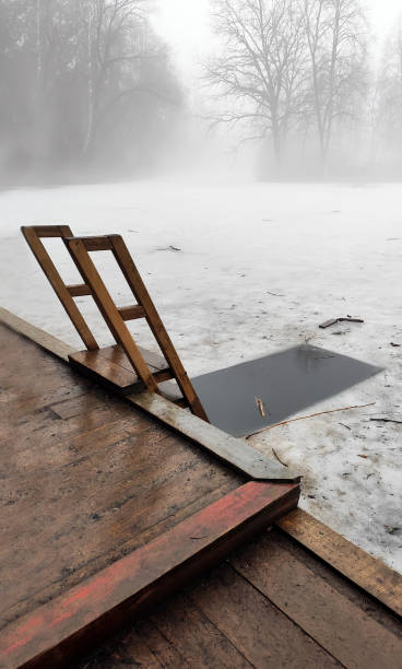 istock Wooden bridge near a lake. Ice hole for bathing. Winter or spring season. Tight fog. 1249363473