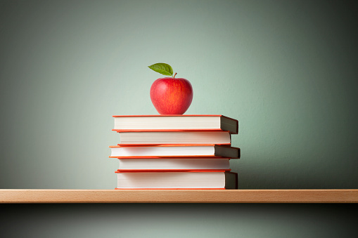 Stack of books with a red apple on the shelf.