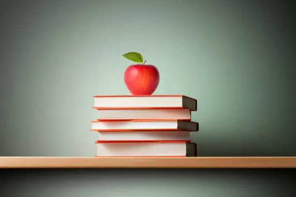 Photo of Stack of books with a red apple on the shelf