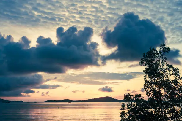 A tropical island on the horizon of the Andaman sea is dwarfed by storm clouds at Dawn.  Sunlight reflects on the water.  Nature background.  Location is Ko Por, Krabi province, Thailand.