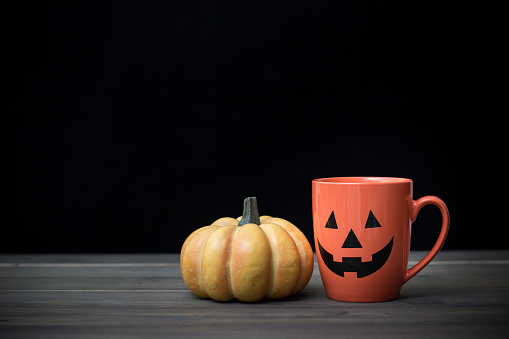 Coffee cup as jack o lantern pumpkin on wooden table. Halloween concept